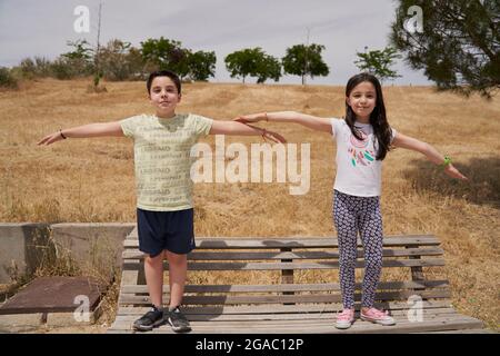 MOSTOLES, SPAIN - May 22, 2021: Happy children playing laughing up on wooden bench with arms crossed in a park Stock Photo