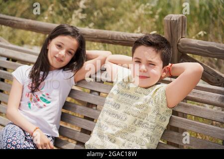 MOSTOLES, SPAIN - May 22, 2021: Children sitting on wooden bench laughing relaxed in park Stock Photo