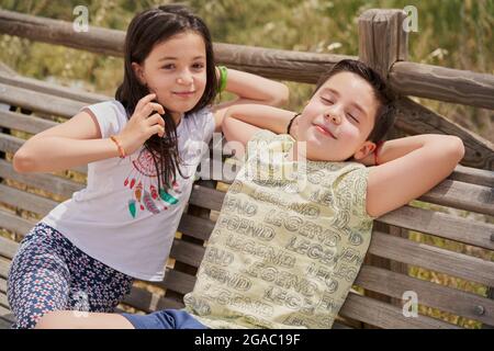 MOSTOLES, SPAIN - May 22, 2021: Children sitting on wooden bench laughing relaxed in park Stock Photo