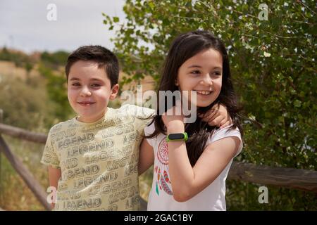 MOSTOLES, SPAIN - May 22, 2021: Children embraced smiling happily in a park with wooden fence behind them Stock Photo