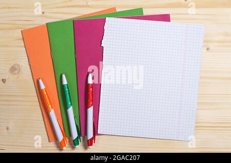 Three colored pens, school notebooks and empty sheet on wooden desk, top view. Space for text Stock Photo