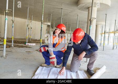 Architects team with a floor plan together during the construction planning on the construction site in the shell Stock Photo