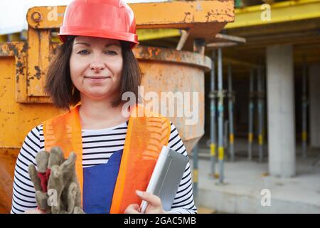 Woman as a craftsman with red hard hat and tablet computer on the building site in the shell Stock Photo