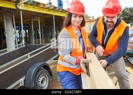 Craftsmen team with hard hats unloading lumber in front of the building site of the house Stock Photo