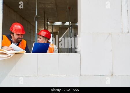 Architect with checklist and foreman discuss construction project on the construction site in the shell Stock Photo