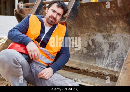 Craftsman or worker on the construction site sits exhausted on an excavator shovel during a break Stock Photo