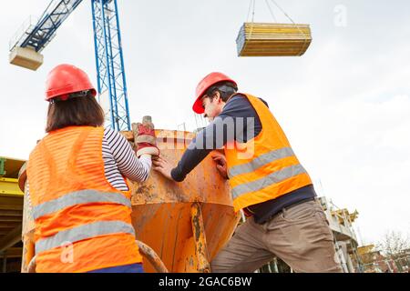 Construction workers work together on cement mixer with lumber on construction crane in the background Stock Photo