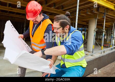 Craftsmen and construction workers with building drawings together in front of a new building as a shell Stock Photo