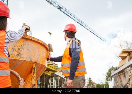 Workers team on the construction site of the new building at the cement mixer with construction crane in the background Stock Photo