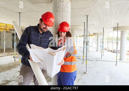 Architect with construction drawing and workers together in the construction planning in the shell of the construction site Stock Photo
