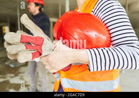 Craftsman or worker with red hard hat and work gloves on a construction site Stock Photo
