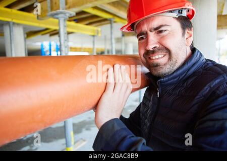 Craftsman on the construction site in the shell transports a plastic water pipe for installation Stock Photo