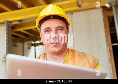 Smiling construction worker as a foreman with tablet computer on the building site of the house Stock Photo