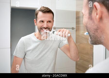 Man brushing his teeth in the bathroom. White teeth and a beautiful smile, morning hygiene concept Stock Photo