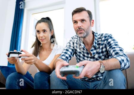 Couple playing computer games, playing the console, holding pads in their hands Stock Photo