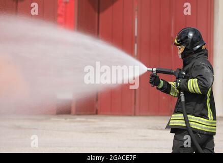 brave firefighter with helmet and uniform extinguishing a car fire using a special white flame retardant foam Stock Photo