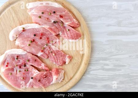 raw pork chops seasoned with different peppers on a wooden cutting board Stock Photo