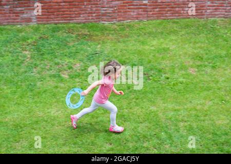 little girl is playing frisbee on the grass in the garden of their house. Selective Focus Girl. Stock Photo