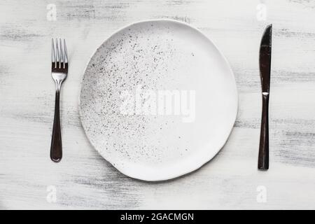 Flat lay of a white spotted plate with silverware place setting over a rustic wood table. Stock Photo