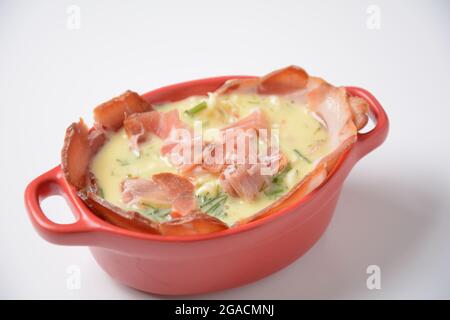 Proсess of cooking Omelette  with bacon, grated parmesan and greens. Raw beaten egg yolks  with ingredients in ceramic cocotte Stock Photo