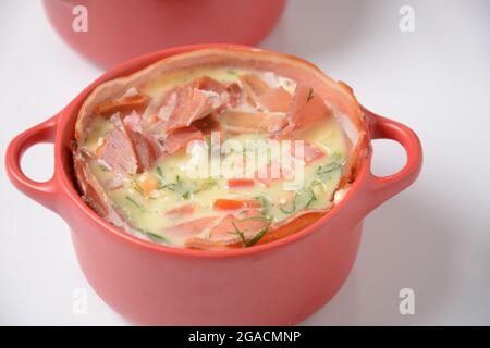 Proсess of cooking Omelette  with bacon, grated parmesan and greens. Raw beaten egg yolks  with ingredients in ceramic cocotte Stock Photo