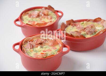 Proсess of cooking Omelette  with bacon, grated parmesan and greens. Raw beaten egg yolks  with ingredients in ceramic cocotte Stock Photo