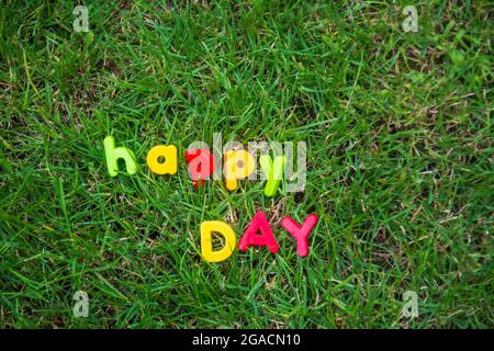 happy day lettering written with toy letters on the grass in the garden of the house Stock Photo
