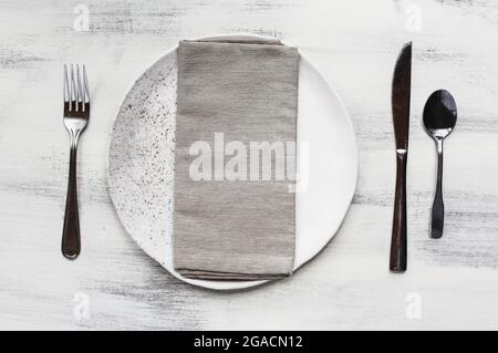 Flat lay of a white spotted plate with napkin and silverware place setting over a rustic wood table. Stock Photo