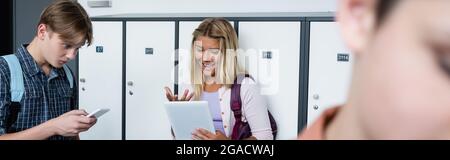excited girl gesturing while using digital tablet near classmate with smartphone, banner Stock Photo