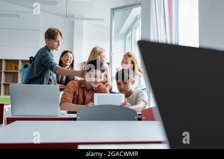 Interracial schoolkids using digital tablet near laptops and friends Stock Photo