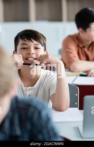 Smiling asian schoolboy holding pen in classroom Stock Photo