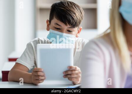 Asian schoolboy in medical mask using digital tablet in classroom Stock Photo