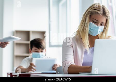 Schoolgirl in medical mask using laptop during lesson Stock Photo