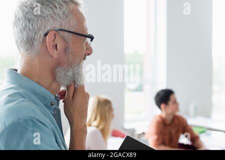 Mature teacher standing near blurred pupils in classroom Stock Photo