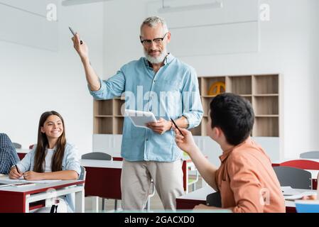 Teacher with marker and digital tablet standing near pupils Stock Photo