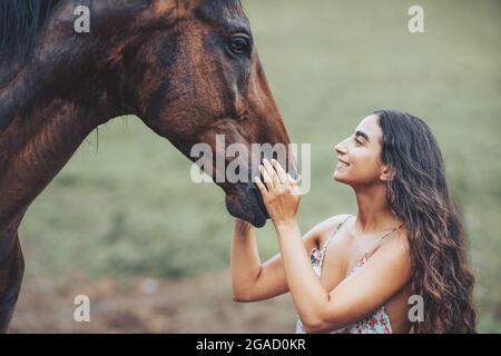Portrait of woman and horse outdoors. Woman stroking a horse. Stock Photo