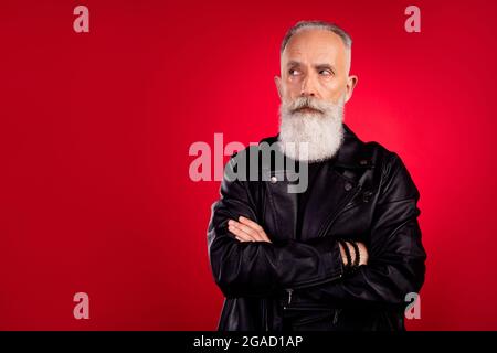 Photo of serious confident old man look empty space crossed hands wear leather jacket isolated on red color background Stock Photo