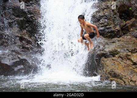 Boy jumping from rock into water in waterfall Stock Photo