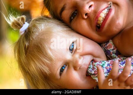 Laughing multicultural kids. Two smiling sisters - swarthy teenage girl and blonde infant baby - emotional portraits. Happy childhood. Preschool age c Stock Photo