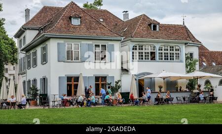 Fondation Beyeler garden cafe building coffee house with people sitting under white umbrellas in the park near the museum. Stock Photo