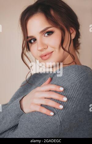 Young female wering warm knitted sweater and looking at camera against beige background Stock Photo