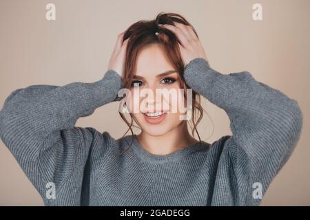 Young female wering warm knitted sweater and looking at camera against beige background Stock Photo