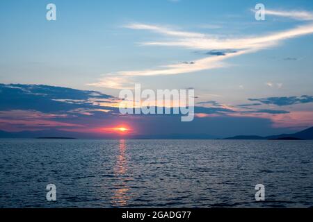 Red and blue sunset with layer clouds over the Mediterranean Sea, seen from Xero Bay on Chersonisi Island, Marmari, Greece. Stock Photo