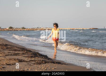 A cheerful and vital woman, in her 70s, walks on a beach at sunset, on the shores of the Mediterranean Sea, Spain Stock Photo