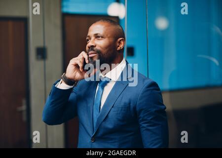 Portrait smiling african american businessman in blue suit in office with mobile phone speaking talking smiling Stock Photo