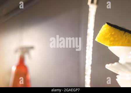 Kitchen sink with water flow and unwashed dishes with yellow sponge on it, copy space, selective focus Stock Photo