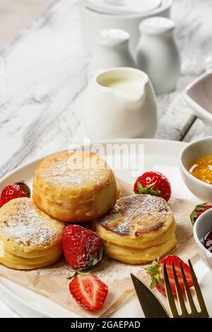 Vertical shot Cottage Cheese Pancakes with fresh strawberries and jam. Curd Cheese Pancakes on a white plate sprinkled with powdered sugar. Delicious Stock Photo
