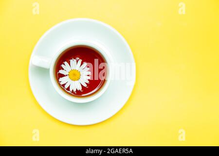 Chamomile tea in a white mug on a yellow background. Means for relaxation, calming tea. Stock Photo