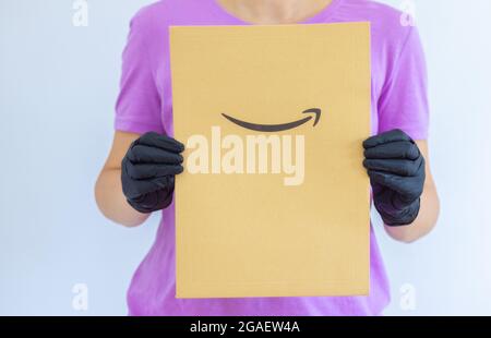 A woman's hand holds in medical gloves a paper envelope Amazon on white background. Express delivery. The courier brought the package  Stock Photo
