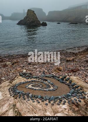 Stone or rock sculpture spiral pattern on the beach with a sea stack on a foggy day, Dunbar, East Lothian, Scotland, UK Stock Photo